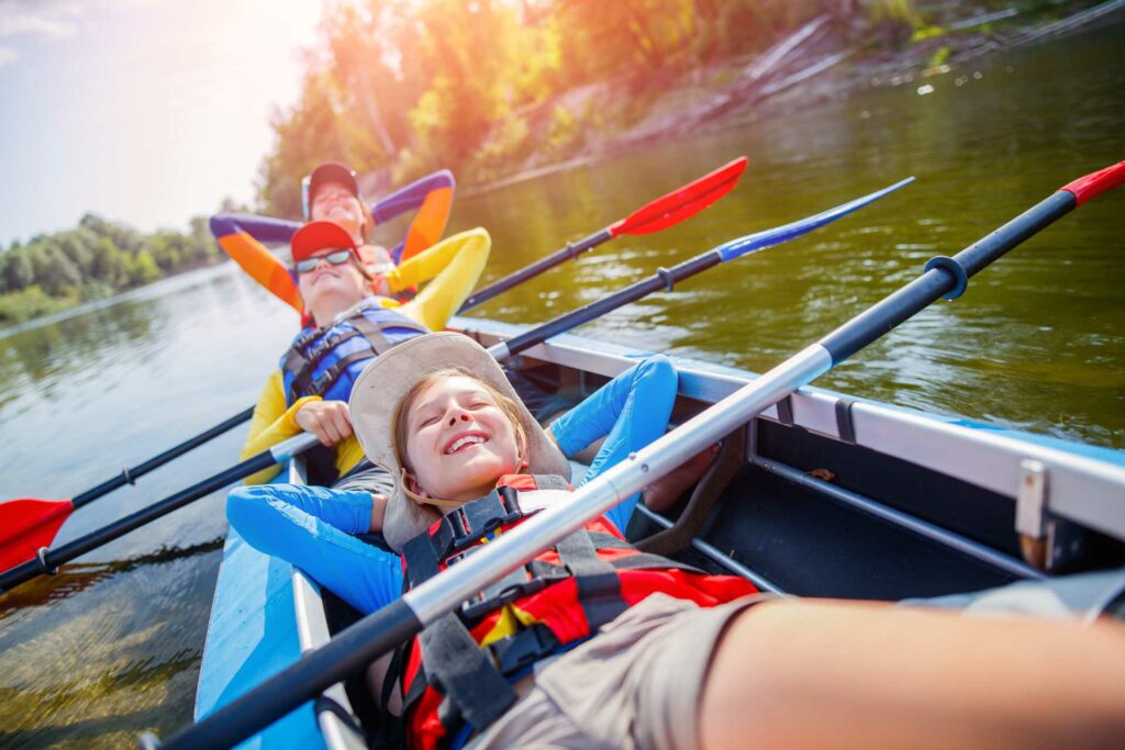 Happy kids kayaking on the river. Active boy with his sisters having fun and enjoying adventurous experience with kayak on a sunny day during summer vacation